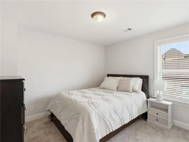 A well-lit bedroom features plush carpeting and a large window providing ample natural light.