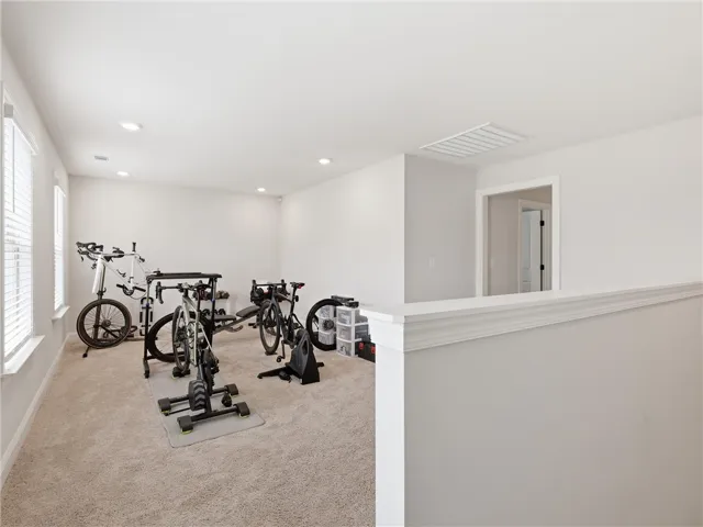 A well-lit exercise room, featuring soft carpeting and bright window light, is ready for a home gym.