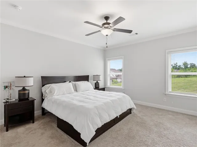 A tranquil primary bedroom with soft carpet, a dark wood bed, and large windows inviting natural light.