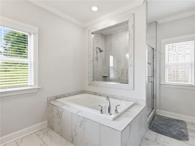 Unwind in a luxurious primary bath featuring a spacious soaking tub and a sleek, glass-enclosed shower.