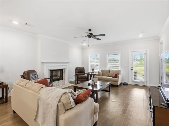 A well-appointed great room features a fireplace, ceiling fan, and rich hardwood floors leading to a glass-paneled exterior door.