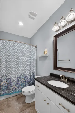 A well-appointed bathroom features a single vanity with stone counters and a shower with a patterned curtain.