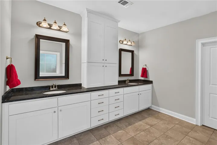 Dual vanities with dark granite counters and clean white cabinetry offer ample storage in this well-appointed bath.