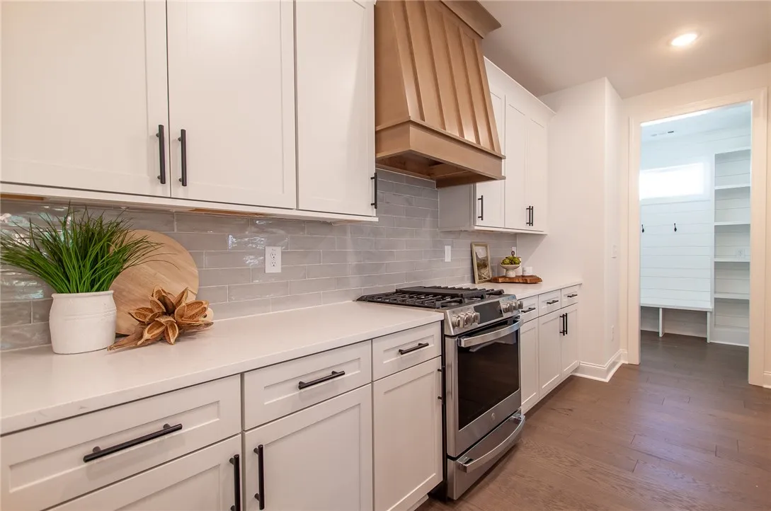 A well-appointed kitchen features a gas range and sleek countertops, with a glimpse of a convenient mudroom. Photos are not of subject property. Photos are of the same floorplan of a completed home.