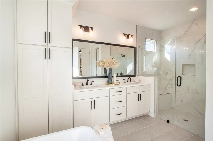 Dual vanities and a spacious glass-enclosed shower create a serene bathing experience. Photos are not of subject property. Photos are of the same floorplan of a completed home.