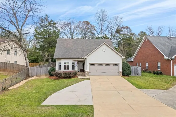 A charming stucco home welcomes with a concrete driveway and an attached garage.