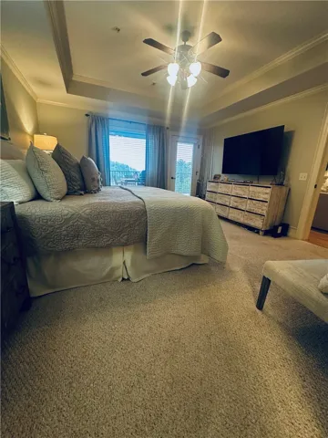 A private balcony extends this serene bedroom, featuring tray ceilings and soft carpeting.