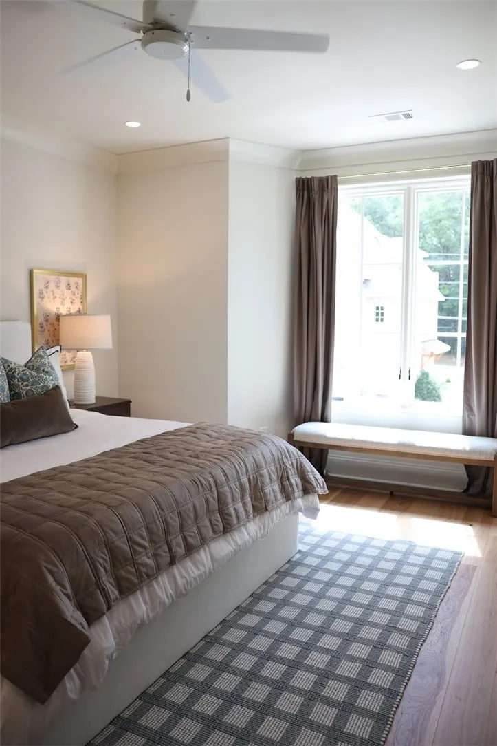 Rich hardwood flooring and crown molding frame this bedroom, while a tall window invites daylight.