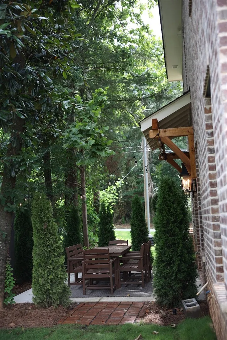A secluded stone-paved patio nestles alongside a classic brick exterior framed by dense mature trees.