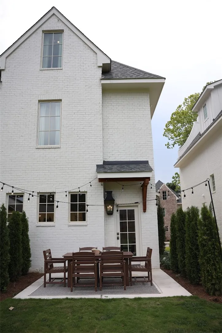 A neat concrete patio accents the rear brick exterior, framed by tidy privacy hedges.