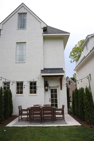 A neat concrete patio accents the rear brick exterior, framed by tidy privacy hedges.