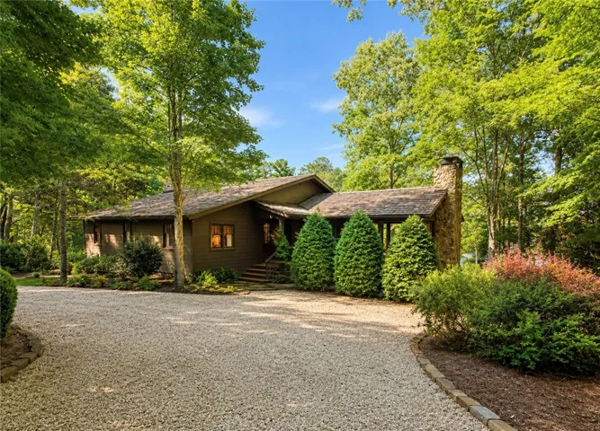 A winding gravel driveway leads to a secluded residence enveloped by natural woodlands and manicured greenery.