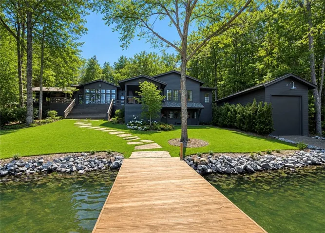 Lakeside home featuring a private dock, lush lawn, and elegant stone pathway.