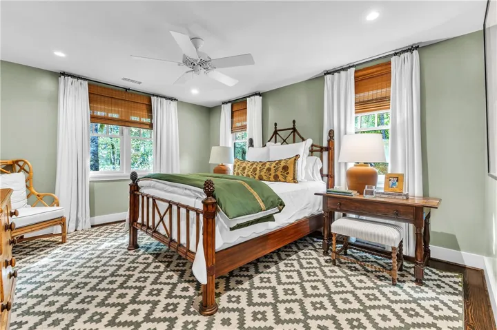An inviting sleeping space with recessed lighting and a ceiling fan, featuring rich hardwood floors peeking from under an area rug.