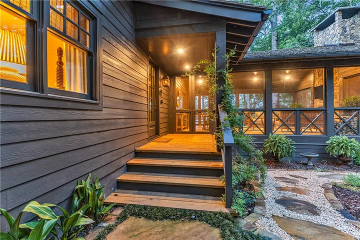 A welcoming front porch with natural wood accents and stone steps leading to a screened-in living area.