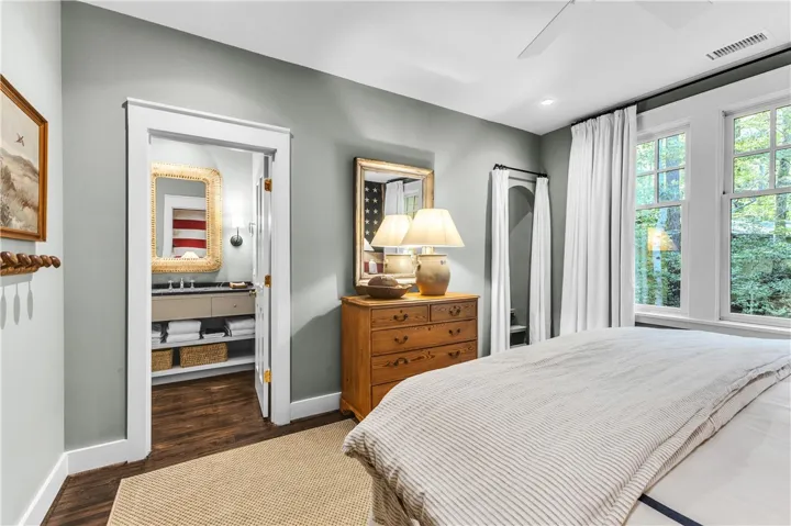 A tranquil primary bedroom with rich wood flooring and ample natural light from large windows.