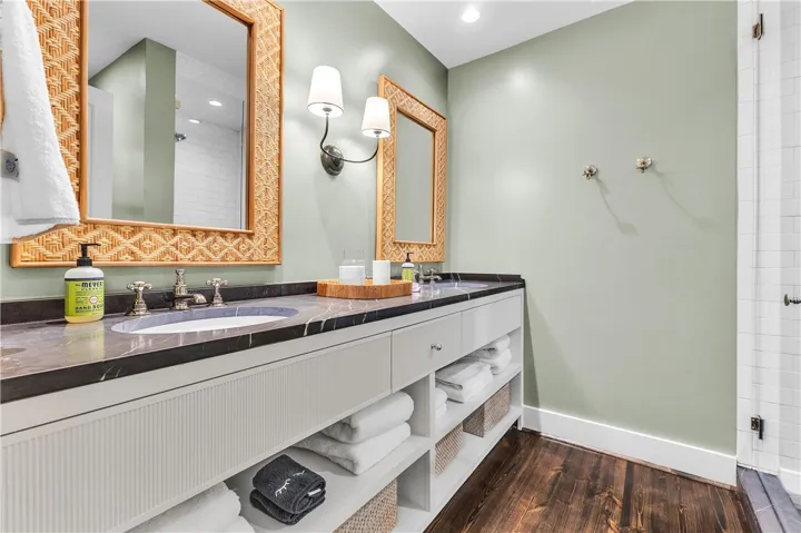 A refined bathroom featuring a long double vanity with elegant black stone countertops and rich hardwood flooring.