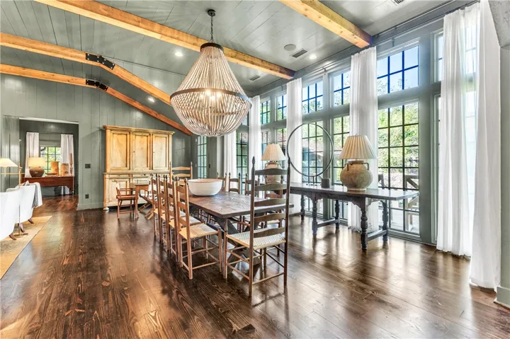 Grand dining room features abundant natural light and rich wood flooring under a striking chandelier.