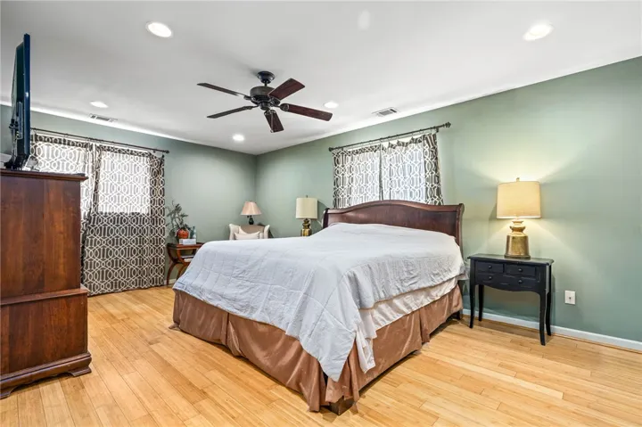 Hardwood floors and a ceiling fan enhance this naturally illuminated sleeping space.