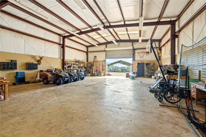 A spacious, high-ceilinged workshop with a large roll-up door opening to a covered outdoor area.