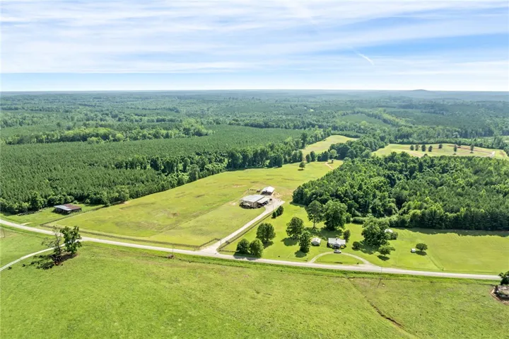Sprawling green fields meet dense woodlands, showcasing a serene, expansive rural landscape.