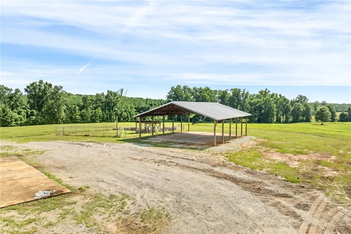 A spacious covered structure offers versatile utility amidst verdant fields and a backdrop of mature trees.