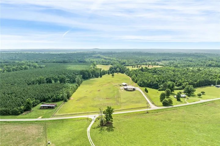 Vast green acreage unfolds, offering serene rural living with a blend of pasture and wooded privacy.