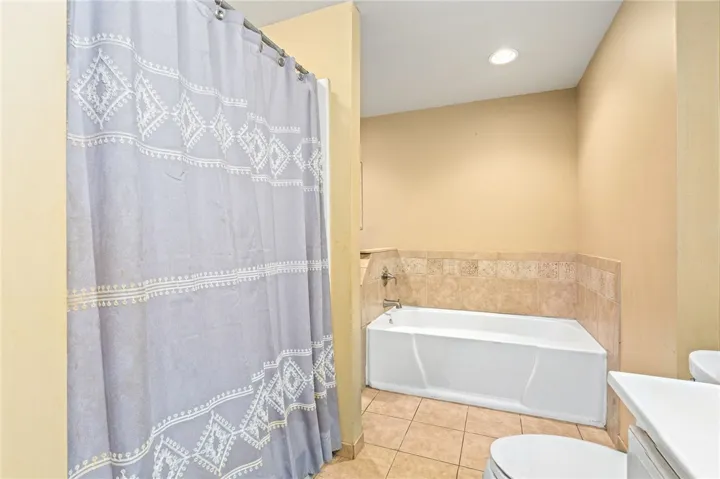 A well-lit bathroom features a built-in tub with tile surround and durable tile flooring.