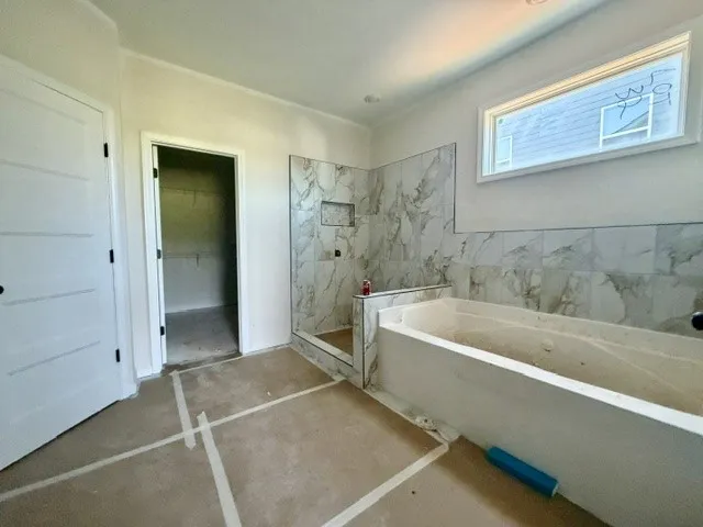 A well-lit primary bathroom featuring a soaking tub, a tiled shower, and a walk-in closet.