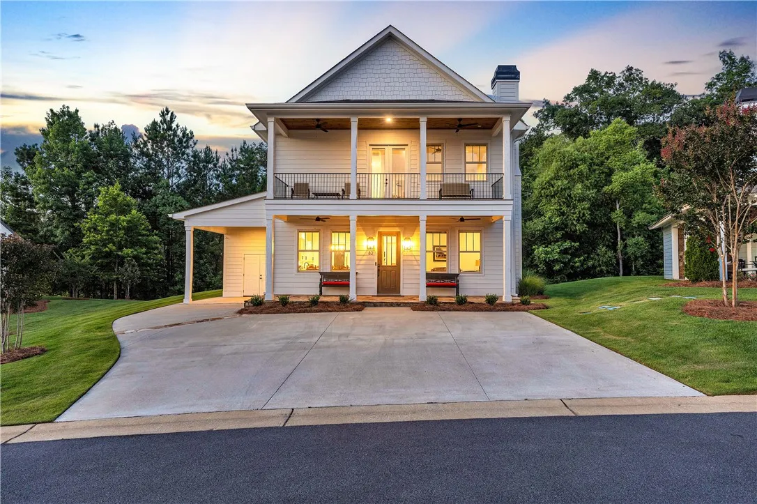 A charming two-story facade with twin balconies, framed by lush greenery and a spacious concrete driveway.