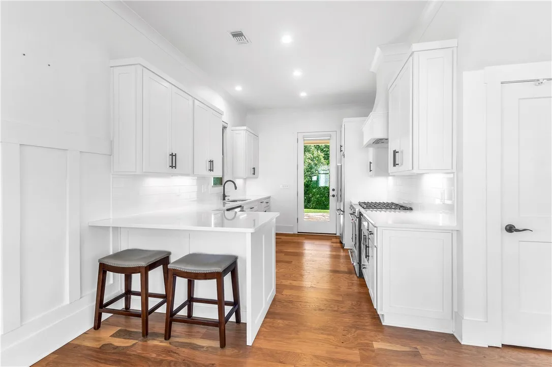 A pristine white kitchen features a breakfast bar, ample cabinetry, and rich hardwood flooring.