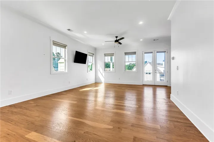 Natural light drenches this spacious living area, showcasing lustrous hardwood flooring and convenient French doors.