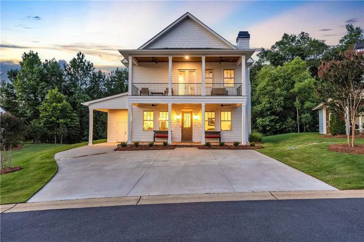 A charming two-story facade with twin balconies, framed by lush greenery and a spacious concrete driveway.