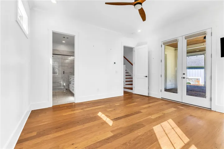 Natural wood flooring complements white walls, creating an airy and adaptable space with a ceiling fan and a view to the outdoors.