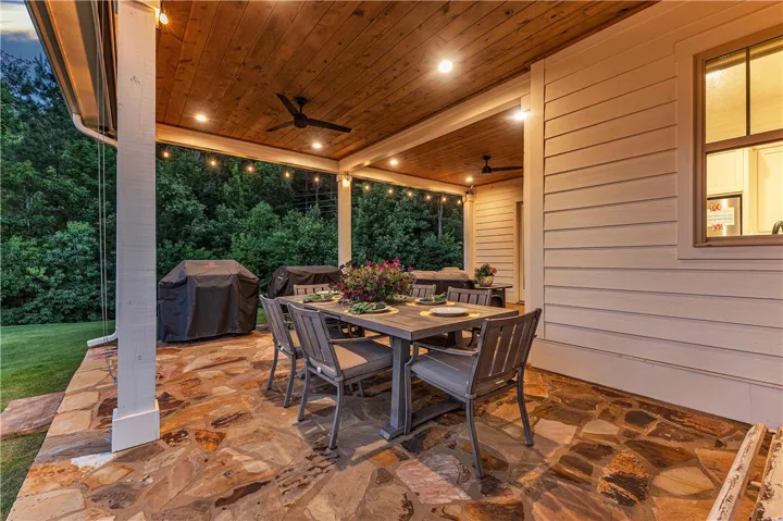 An inviting outdoor living area awaits with flagstone flooring, a wooden ceiling, and ample space for dining and grilling.