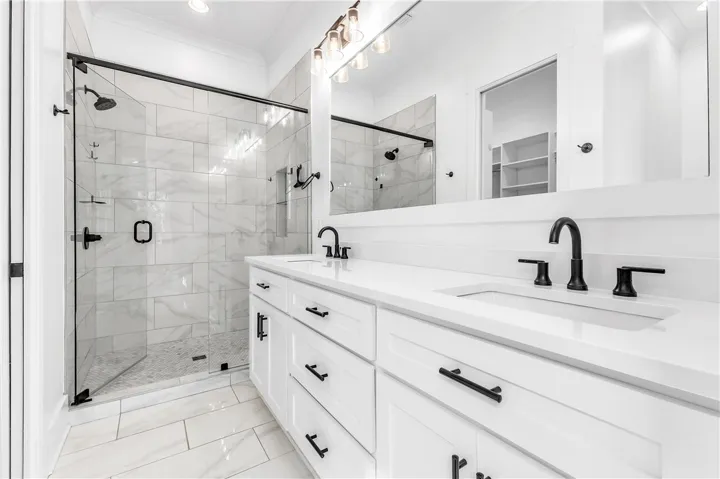 A well-lit primary bathroom features a double vanity and a glass-enclosed shower with subway tile.