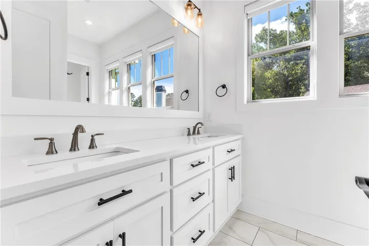 A well-lit bathroom features white cabinetry with modern black hardware and a long, integrated mirror reflecting outside views.