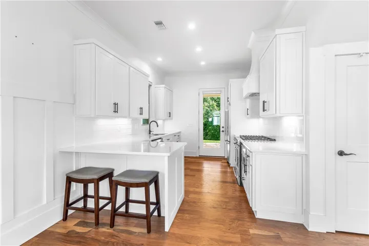 A pristine white kitchen features a breakfast bar, ample cabinetry, and rich hardwood flooring.