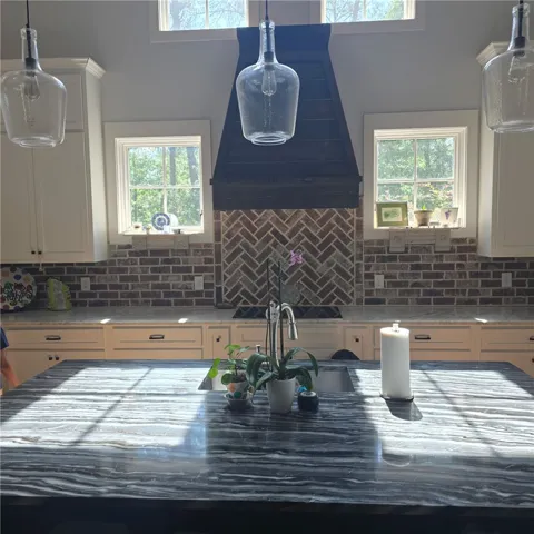 A well-lit kitchen boasts elegant countertops and a distinctive brick backsplash, creating an inviting space.