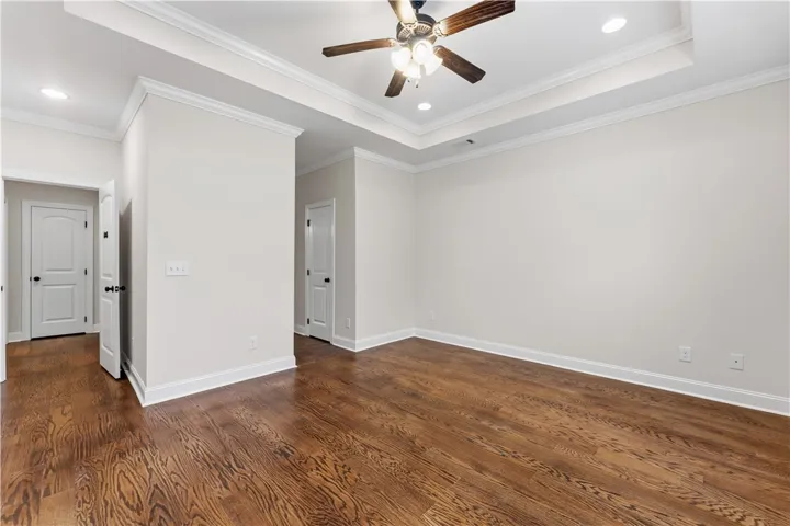Rich hardwood flooring complements the detailed crown molding and tray ceiling in this spacious bedroom.