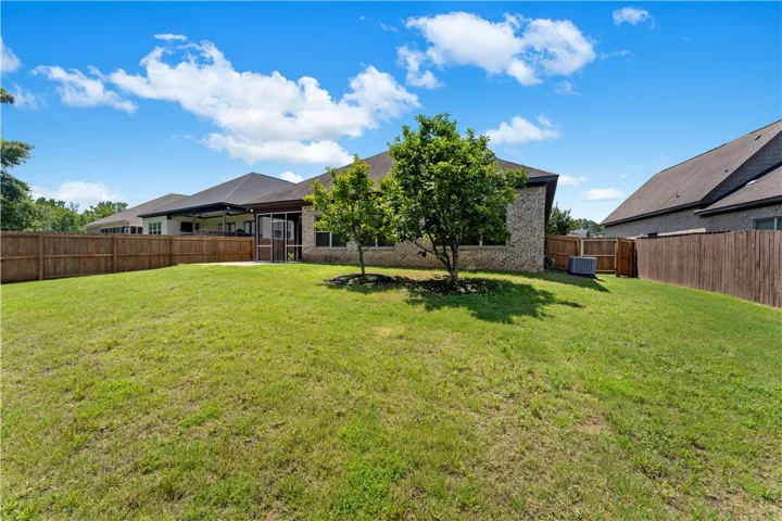 A vast green yard wraps around a brick home, featuring a screened porch and mature trees for natural shade.