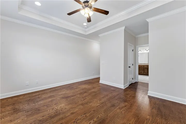 Hardwood floors and a tray ceiling with a fan define this inviting primary bedroom.