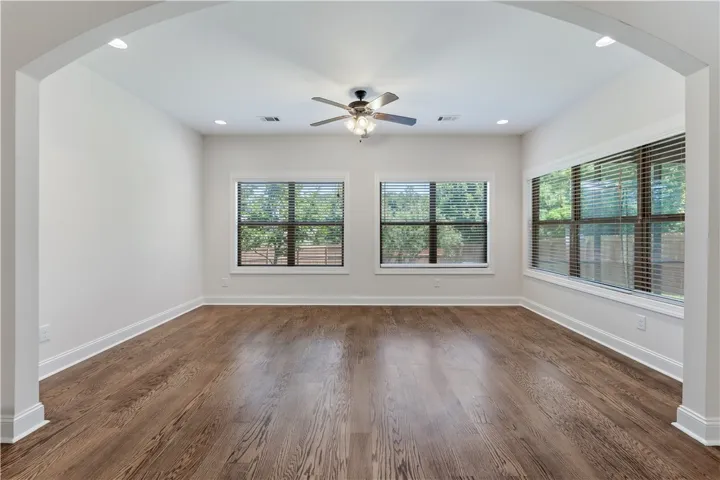 Natural light streams through multiple windows in this well-lit living area, highlighting the rich hardwood flooring.