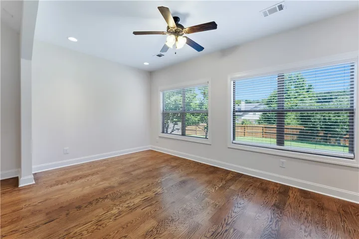 Well-lit room with richly toned hardwood floors and views of mature trees from wide windows.