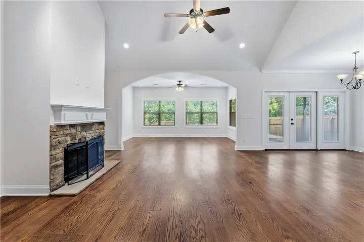A spacious living area showcasing rich hardwood floors and a cozy stone fireplace, extending to a bright sunroom.