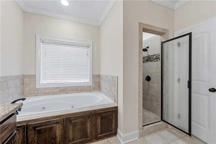 Relax and unwind in this primary bathroom featuring a spacious soaking tub and a separate glass-enclosed shower.