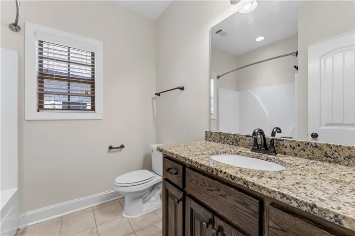 A pristine bathroom featuring a vanity with granite counters and tile flooring.