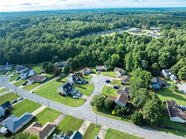 An aerial perspective reveals a peaceful suburban neighborhood surrounded by vast, verdant woodland.