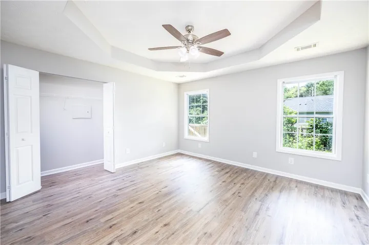 A spacious bedroom features tray ceilings, a ceiling fan, and ample natural light.