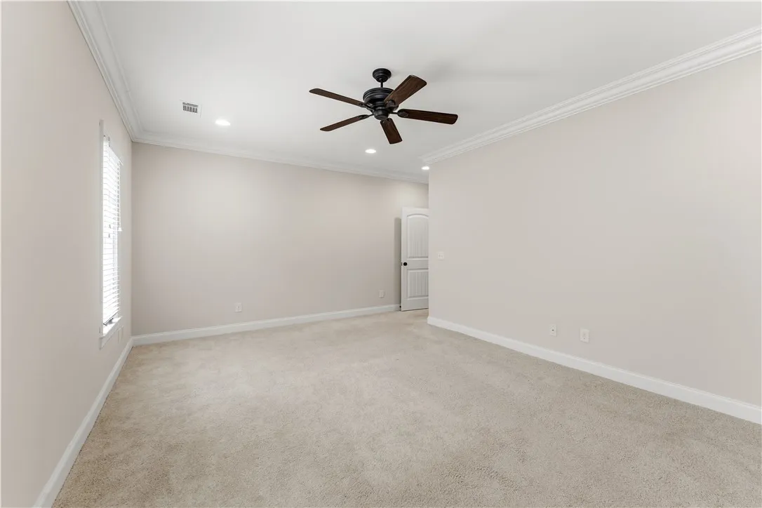 A spacious, naturally illuminated room featuring a ceiling fan and plush carpeting.